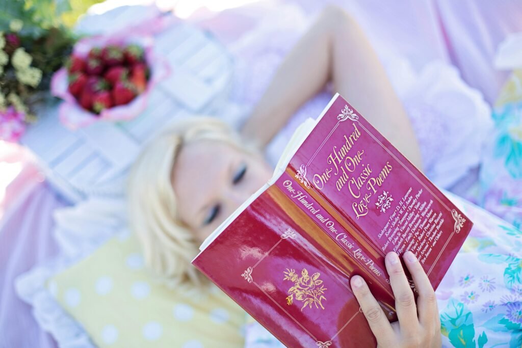 Blonde woman enjoying leisure time reading a love poems book outdoors on a sunny day.